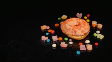 Turuncu komik sürpriz sırlı çörek ile sprinkles, çizgili karamelli şeker, Kuru üzüm veya fıstık içinde renkli badem döndürmek siyah arka plan üzerine