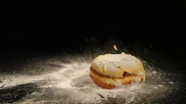 Een donut met een poeder suiker valt op een zwart Bureau — Stockvideo