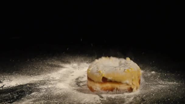 Ein Donut mit Zuckerpuder fällt auf einen schwarzen Schreibtisch — Stockvideo