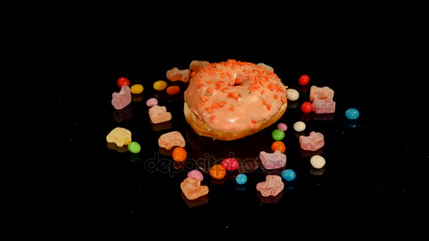 Oranžové vtipné překvapení prosklené kobliha se sype, pruhované karamelové bonbóny, barevné dragee rozinky nebo oříšky uvnitř otočit na černém pozadí — Stock video