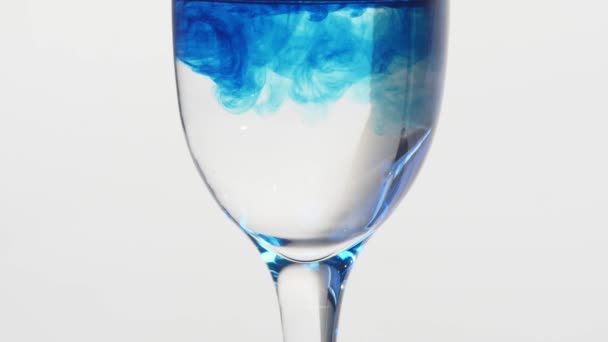 Tinta azul cayendo en un vaso de agua sobre un fondo blanco. El veneno en el concepto de vidrio . — Vídeos de Stock