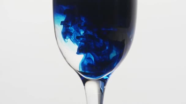 Blaue Tinte tropft in ein Glas Wasser auf weißem Hintergrund. das Gift im Glaskonzept. — Stockvideo