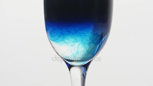 Encre bleue tombant dans un verre d'eau sur fond blanc. Le poison dans le concept du verre . — Video