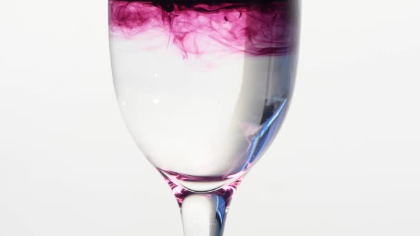 Tinta púrpura cayendo en un vaso de agua corriente — Vídeos de Stock