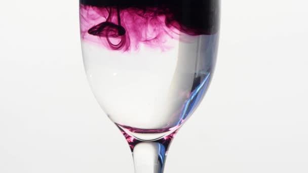 Encre violette tombant dans un verre d'eau plate — Video