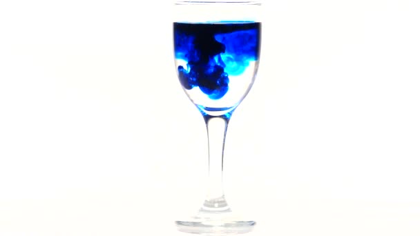 Синие чернила падают в стакан с водой на белом фоне — стоковое видео