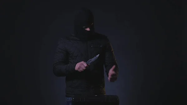 Masked Criminal with a Knife in Darkness. Filmed with low key spot light