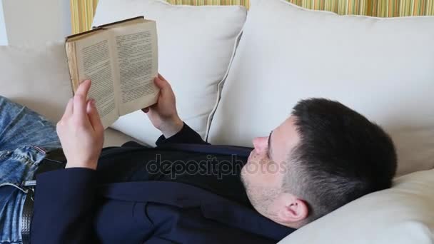 Man reading a book lying on the couch and dreams — Stock Video