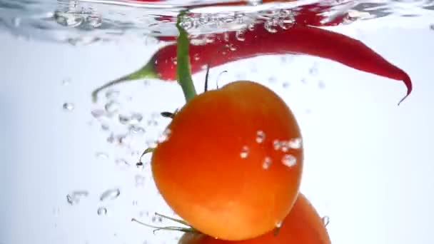 Primer plano de tomate fresco y pimienta cayendo en agua clara con gran salpicadura aislada sobre fondo blanco. Alimentación saludable — Vídeo de stock