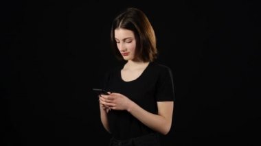 Güzel genç kız bir smartphone kullanarak ve gülümseyerek, koyu arka plan üzerinde duran