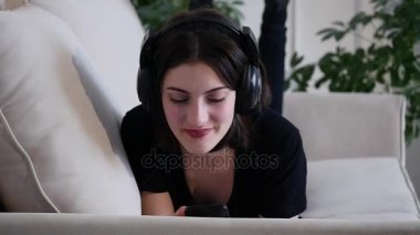 Güzel çekici genç kadın kanepede yatan ve müzik ve gülümseme smartphone ile