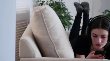 Güzel çekici genç kadın kanepede yatan ve müzik smartphone ile