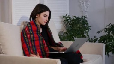 Oturma odasında kanepede otururken kahve içme dizüstü kullanan genç kadın