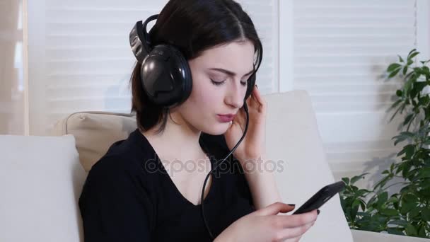 Красива приваблива молода жінка сидить на дивані і слухає музику — стокове відео