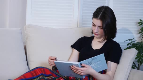 Привлекательная молодая женщина лежит на диване и читает книгу — стоковое видео