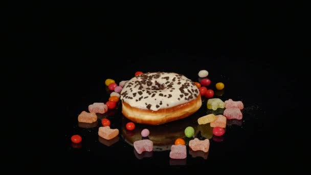 Λευκό αστείο έκπληκτος τζάμια ντόνατ με ψεκάζει, ριγέ καραμέλα καραμέλες, πολύχρωμο dragee με σταφίδες και φιστίκια στο εσωτερικό περιστρέφονται σε μαύρο φόντο — Αρχείο Βίντεο