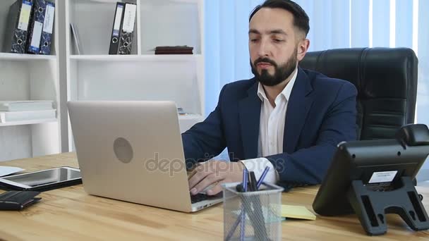Jonge manager zitten aan de balie in heldere kantoor, die op laptop werkt — Stockvideo