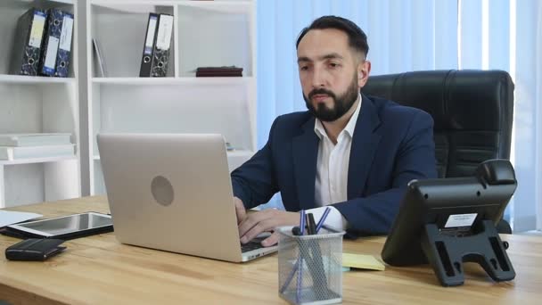 Young manager sitting at desk in bright office, working on laptop — Stock Video