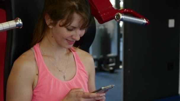 Gelukkig sportieve vrouw schrijven van een bericht op haar mobiel op sportschool — Stockvideo