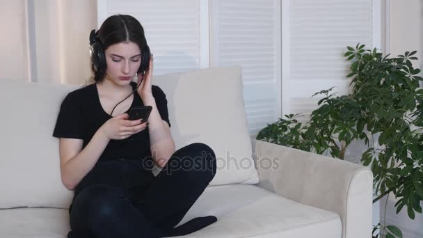 Młoda kobieta słuchać muzyki, siedząc na kanapie w domu 4k — Wideo stockowe