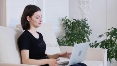 Genç ve güzel kadın laptop ve gülümseme kullanarak kanepede rahatlatıcı