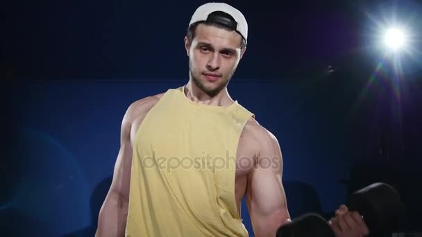 Young muscular built athlete working out in a gym, sitting on a weightlifting machine and lifting two dumbbells — Stock Footage Young muscular built athlete working out in a gym, sitting on a weightlifting machine and lifting two dumbbells Royalty Free Stock Footage