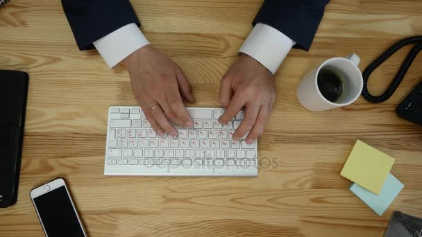 Draufsicht auf den Schreibtisch mit Büromaterial. Mann tippt auf seinem Laptop und trinkt Kaffee — Stockvideo