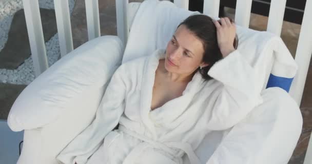 Сексуальна і красива жінка спокійно відпочиває в кріслі, одягненому в халат — стокове відео
