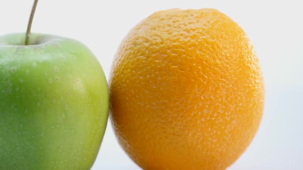 Uma laranja e uma maçã verde. A fruta está girando lentamente sobre um fundo branco — Vídeo de Stock