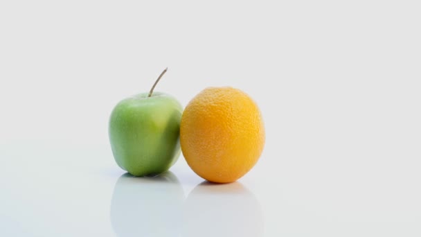 Une orange et une pomme verte. Le fruit tourne lentement sur un fond blanc — Video