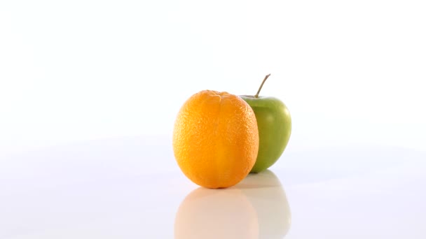 Une orange et une pomme verte. Le fruit tourne lentement sur un fond blanc — Video