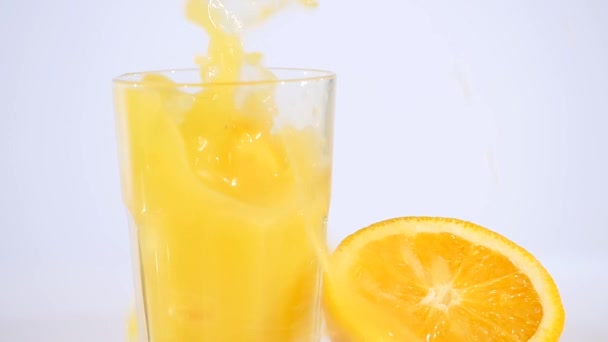 Orange juice pouring in glass on color background — Stock Video