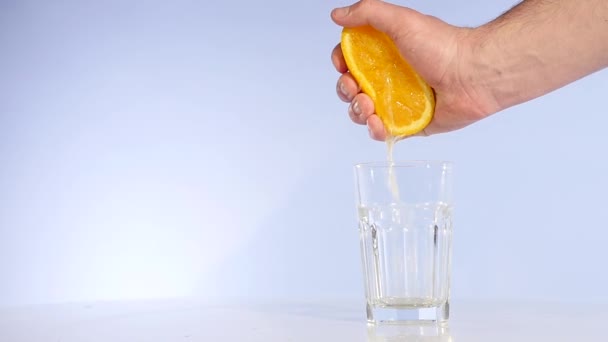 Mano exprimiendo jugo de naranja en un vaso de agua en cámara lenta — Vídeos de Stock