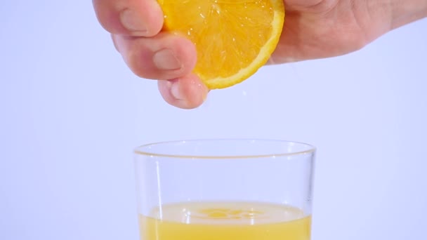 Mano exprimiendo jugo de naranja en un vaso de agua en cámara lenta — Vídeos de Stock