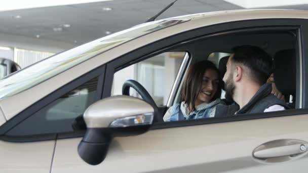 Посещение автосалона. Beautiful family is talking and smiling while sitting in their new car. молодой человек показывает пальцем вверх — стоковое видео