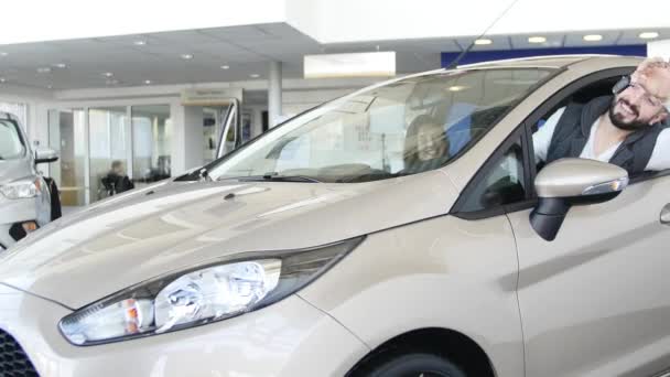 Un hombre feliz mostrando la llave de su auto nuevo. Auto negocio, venta de coches, la tecnología y el concepto de la gente - macho feliz con concesionario de automóviles en el salón de exposición o auto. Joven con un vendedor en un espectáculo de motor — Vídeo de stock