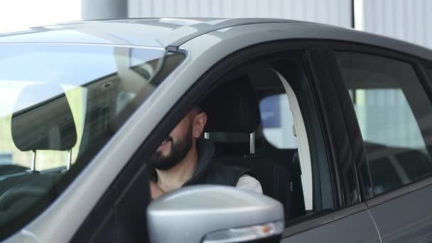 Odwiedź salon. Młody człowiek łapie kluczyki do samochodu, patrząc na kamery i uśmiechnięty, siedzi w jego nowy samochód — Wideo stockowe