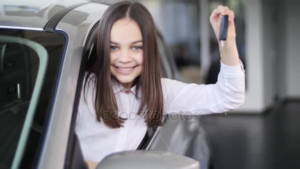 Niña feliz mostrando la llave de su auto nuevo. Auto negocio, venta de coches, la tecnología y el concepto de la gente - macho feliz con concesionario de automóviles en el salón de exposición o auto. Joven con un vendedor en un espectáculo de motor — Vídeos de Stock