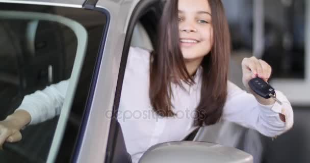 행복 한 아기 소녀는 그의 새로운 자동차의 키를 보여주는. 자동차 사업, 자동차 판매, 기술 및 사람들 개념-자동 표시 또는 살롱에 자동차 딜러와 함께 행복 한 남자. 젊은 남자는 모터쇼에서 세일즈 맨으로 — 비디오