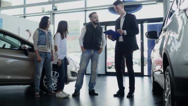 Vendedor de coches muestra a una familia joven información sobre su nuevo coche — Vídeos de Stock