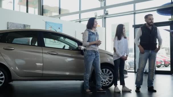 Vendedor de coches muestra a una familia joven información sobre su nuevo coche — Vídeos de Stock