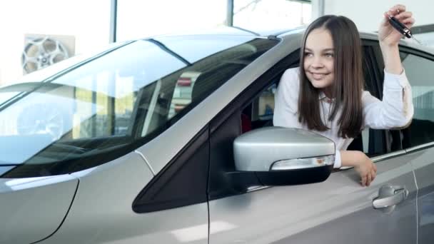 Niña feliz mostrando la llave de su auto nuevo. Auto negocio, venta de coches, la tecnología y el concepto de la gente - macho feliz con concesionario de automóviles en el salón de exposición o auto. Joven con un vendedor en un espectáculo de motor — Vídeos de Stock