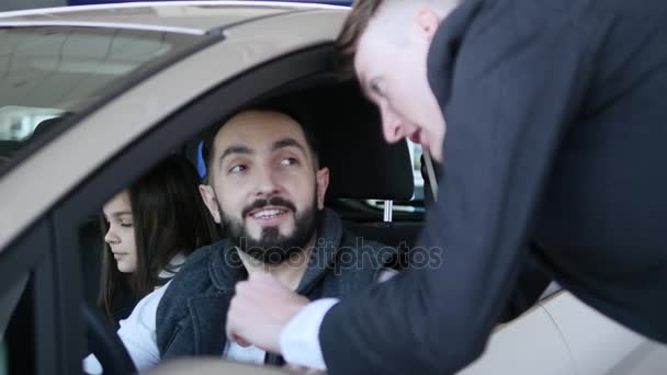 Sala de exposición de coches. Concesionario de vehículos Mostrando Joven coche nuevo. Auto negocio, venta de coches, la tecnología y el concepto de la gente - macho feliz con concesionario de automóviles en el salón de exposición o auto. Joven con un vendedor en un motor — Vídeo de stock