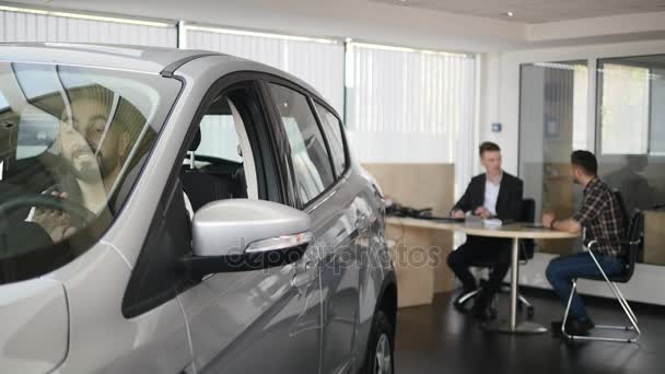 Um homem feliz a mostrar a chave do carro novo. Negócio de automóvel, venda de carros, tecnologia e conceito de pessoas - macho feliz com revendedor de carros em show de automóveis ou salão de beleza. Jovem com um vendedor numa feira de automóveis — Vídeo de Stock