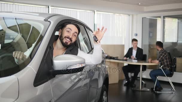 Un homme heureux montrant la clé de sa nouvelle voiture. Entreprise automobile, vente de voitures, technologie et concept de personnes - homme heureux avec concessionnaire automobile dans le salon ou le salon de l'automobile. Jeune homme avec un vendeur dans un salon de l'automobile — Video