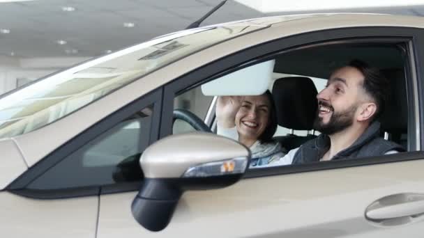 Een bezoek aan een autodealer. Prachtige familie is praten en lachen zittend in hun nieuwe auto. jonge man verschijnt vinger — Stockvideo