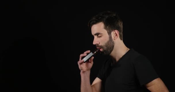 Junger Mann dampft mit einer elektronischen Zigarette und macht ein paar Rauchwolken — Stockvideo