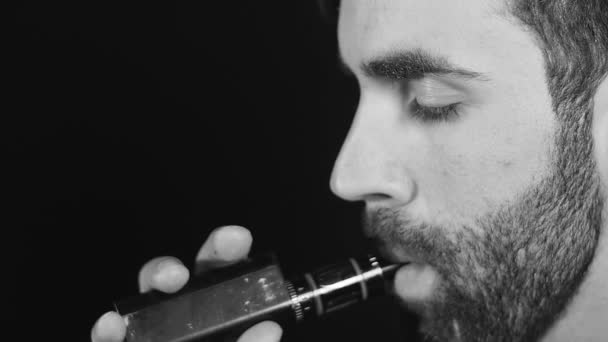 Vaping man holding a mod. A cloud of vapor. Black background Black and white — Stock Video