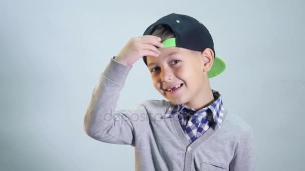 Kid in a cap straightens the forelock and shows the tongue and sticking out tongue isolated on a grey background — Stock Video