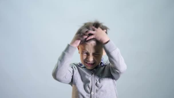 Le garçon en colère froisse ses cheveux sur fond gris — Video